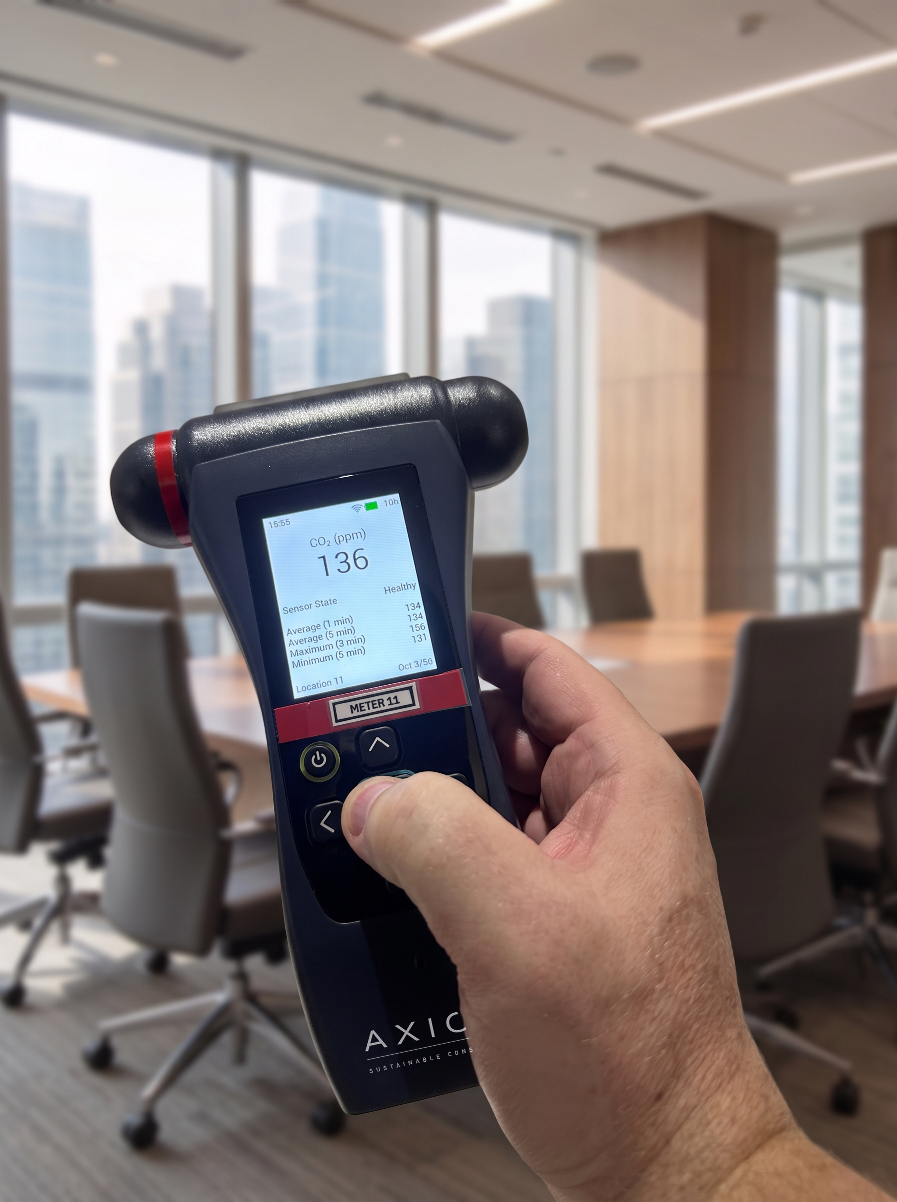 Hand holding an air-quality meter reading 136 ppm CO2 in a corporate boardroom
